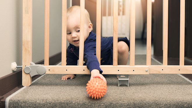 child reaching through baby gate for toy